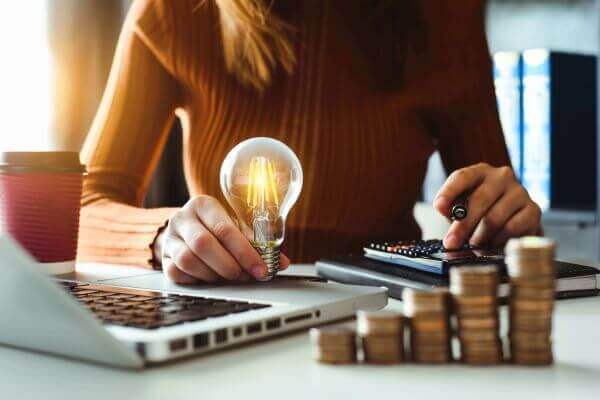 A woman manages her energy bills, while holding a bulb which she appears to be lighting. 
